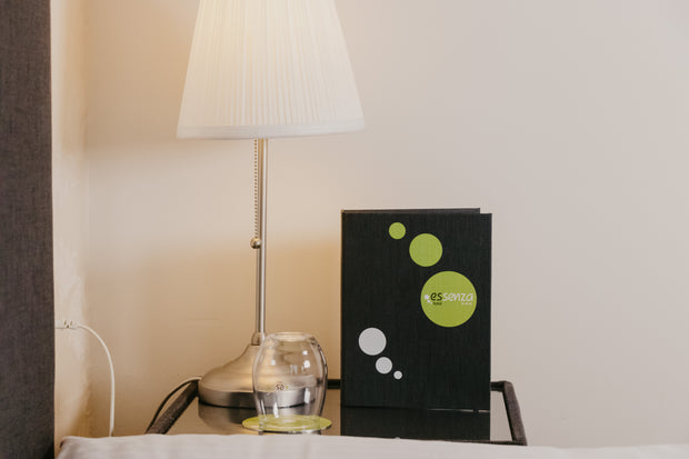 Zwarte menukaart met groen logo op tafel met lamp en glas tegen beige muur